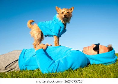 Man Relaxing With Best Friend Dog In Matching Blue Hoody Sweatshirts On Bright Green Grass Meadow