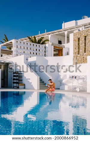 man relaxing in the infinity swimming pool looking at the ocean, young man in the swimming pool relaxing reading a book by the pool. 