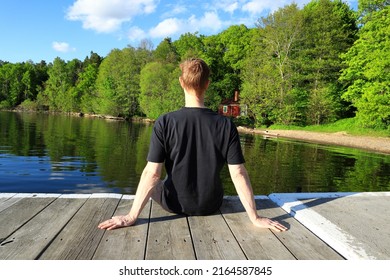 Man relaxing at a lake during the early summer. Green forest in the background. Sitting down on one wooden bridge. Mälaren, Stockholm, Sweden, Europe.