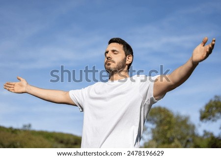 Man relaxing meditating and breathing in nature. Young man with his arms open while breathing and enjoying the sun on a summer day.