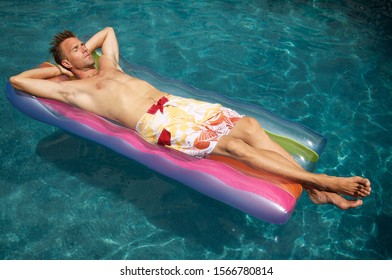 Man relaxing on a colorful inflatable lilo raft floating in a sunny swimming pool - Powered by Shutterstock