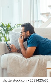 Man relaxing on the couch while using his smartphone to explore social media, watching videos, and connecting with friends, representing a contemporary lifestyle of leisure and digital engagement