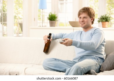 Man Relaxing On Living Room Sofa, Using Remote Control, Having Beer, Smiling.?