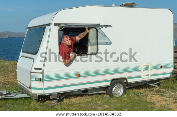 man is relaxing with a travel trailer. caravan\
trailer of large size, equipped with all necessary household\
appliances to ensure the comfort of the traveler. tourist camper,\
recreational vehicle RV.