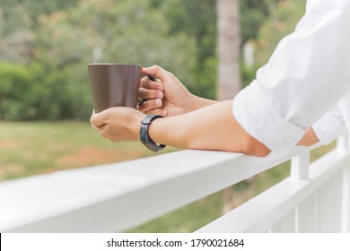 Man relaxjng hand holding coffee mug while standing on balcony.