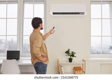 El hombre con control remoto del aire acondicionado crea una temperatura cómoda para él. El joven enciende el aire acondicionado o ajusta el modo de la casa de aire acondicionado. Concepto de sistema climático.