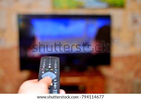 The man with the remote control in hand watching the sports channel and presses the button on the remote control. Remote control in hand closeup.