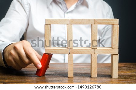 The man removes the red structural element, which will collapse. Destruction of a complex structure by negligence. Incompetent businessman. Loss of key elements and employees. Damage to the opponent.