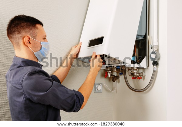 a man repairing\
a boiler in a medical mask