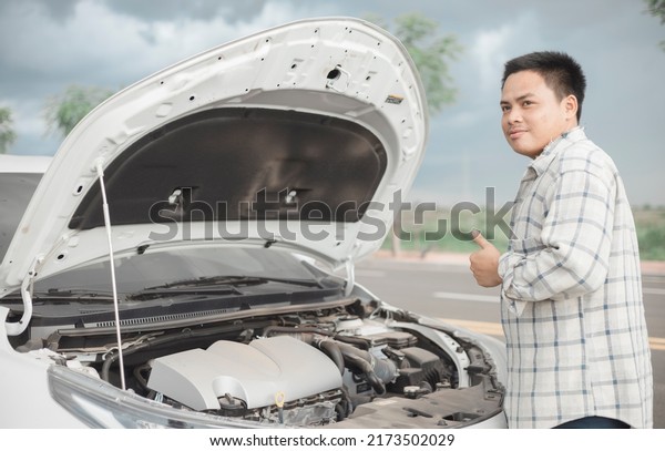 Man repairing a broken car by the road. Man\
having trouble with his broken car on the highway roadside. Man\
looking under the car hood. Car breaks down on the autobahn.\
Roadside assistance\
concept.