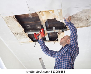 Man repairing collapsed ceiling. Ceiling panels damaged  huge hole in roof from rainwater leakage.Water damaged ceiling . 