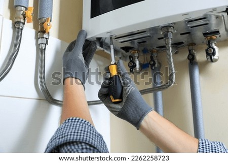 Man repairing gas boiler with screwdriver indoors, closeup