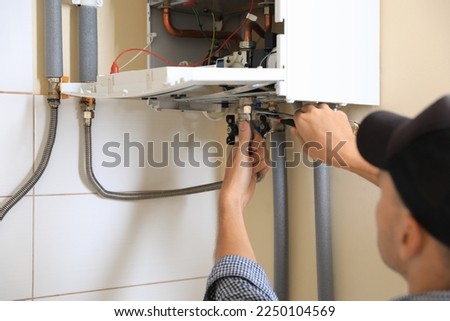 Man repairing gas boiler with waterpump plier indoors, closeup