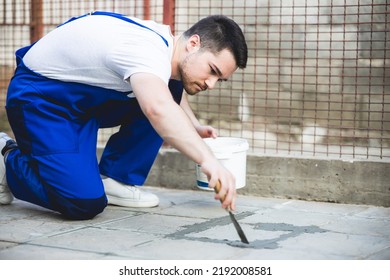 A Man Repairing The Grout On A Tile Floor.