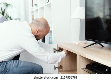 Man Repairing A Loose Cabinet Door Hinge At Home Using A Screwdriver