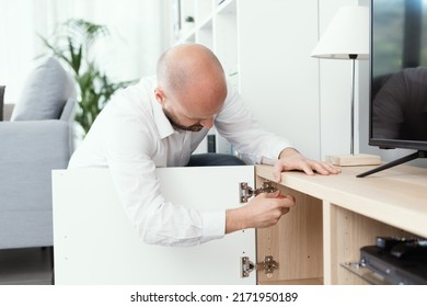 Man Repairing A Loose Cabinet Door Hinge At Home Using A Screwdriver