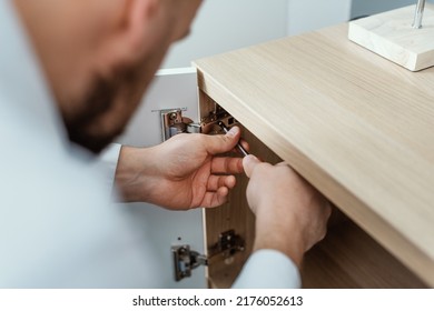 Man Repairing A Loose Cabinet Door Hinge At Home Using A Screwdriver