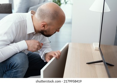 Man Repairing A Loose Cabinet Door Hinge At Home Using A Screwdriver