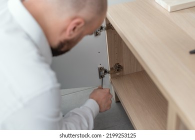 Man Repairing A Loose Cabinet Door Hinge At Home Using A Screwdriver