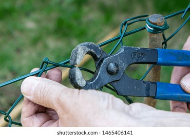 A Man Repairing A Metal Wire Fence With Pliers