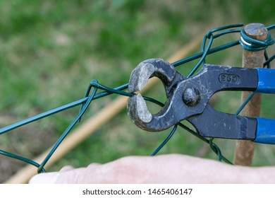 A Man Repairing A Metal Wire Fence With Pliers