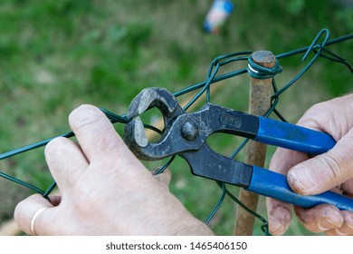 A Man Repairing A Metal Wire Fence With Pliers