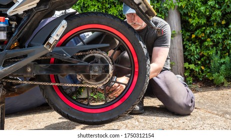 A man repairing a motorbike with bushes in the background