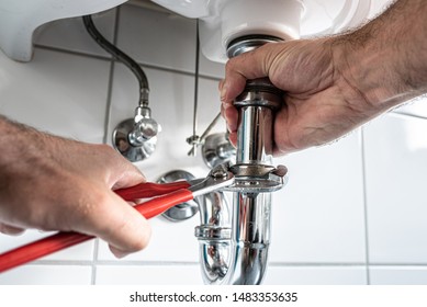 Man Repairing Sink Trap With Adjustable Pipe Wrench In Bathroom