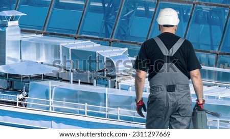 Man repairman. Master near ventilation pipes. Installation of ventilation for buildings. Man repairman with back to camera. Metal ventilation pipes on roof factory. Cleaning ventilation systems