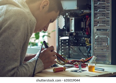 Man repairman is trying to fix using the tools on the computer that is on a workplace in the office. The concept of service electronics and computers.
