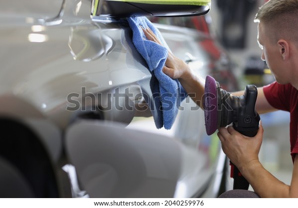 Man repairman wiping car with\
microfiber cloth and holding polishing machine in his hand\
closeup