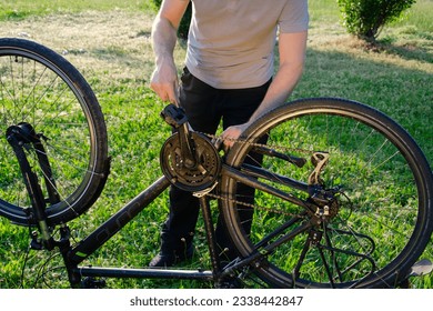 A man repairs a bicycle in the summer in a green park. He's standing behind the bike. - Powered by Shutterstock