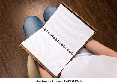 Man rerolls pages in an open notepad with white pages and a wooden brown box-bound cover that lies on his knees