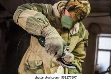 A man in a respirator handles wood grinder. Inside the workshop. Dusty room. - Powered by Shutterstock