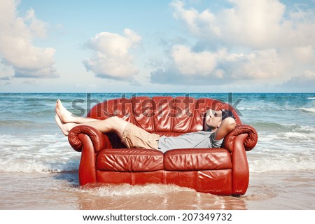 man resting in leather couch on the beach