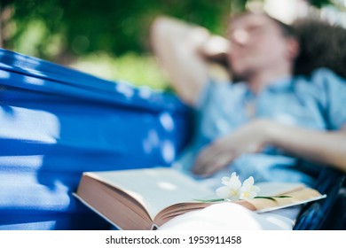 A man is resting and reading in a hammock. Close-up. Day off and relaxation. A young guy lies in a hammock with a book near a country house in the shade on a sunny day