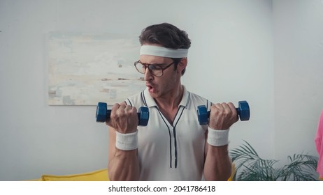 Man In Retro Sportswear And Eyeglasses Lifting Dumbbells At Home