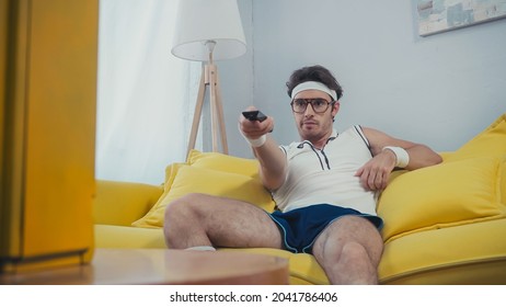 Man In Retro Sportswear Sitting On Yellow Sofa And Switching Channels