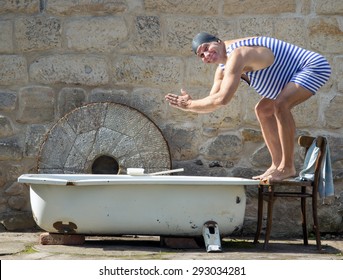 Man in retro swimsuit jumps to the outdoor bathtub. Cheerful swimmer with bathing cap is preparing to swim in the tub.