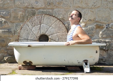 Man In Retro Swimsuit Resting In The Old Outdoor Bathtub.Vintage Style Swimmer Sunbathing In The Tub Outside. Domestic Holiday.