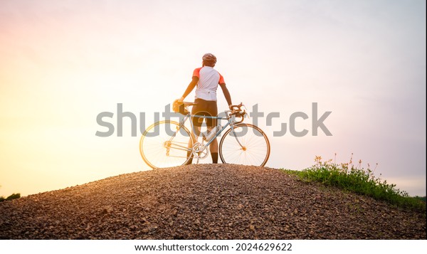 A man ride on bike on the road. Man riding\
vintage sports bike for evening exercise. A man ride bicycle to\
breathe in the fresh air in midst of nature, meadow, forest, with\
evening sun shining through