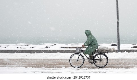 Man Rides A Bicycle In A Snowfall In A Sea Side Road