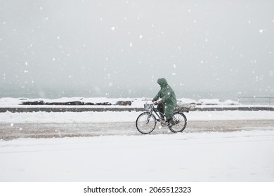 A Man Rides A Bicycle In A Snowfall At The Sea Side Road