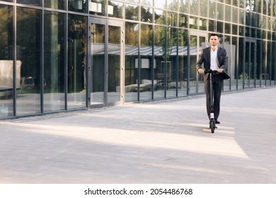 Man rides an electric scooter on the road. Modern way of getting around. Handsome man in a suit riding electric scooter in a city. Adult businessman riding with electric scooter to work - Powered by Shutterstock