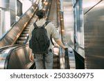 A man rides an escalator up. Urban modern transport. A young guy with a backpack climbs the escalator at a metro station, train station or shopping center