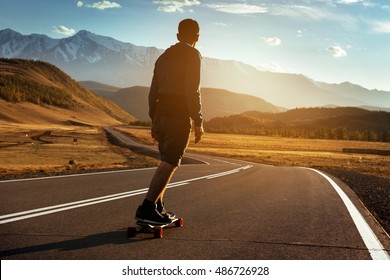 Man rides at straight road on longboard at sunset time