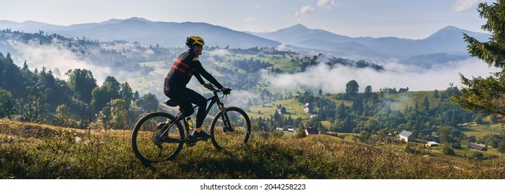 Man riding bicycle on grassy hill and looking at beautiful misty mountains. Male bicyclist enjoying panoramic view of majestic mountains during bicycle ride. Concept of sport, bicycling and nature. - Powered by Shutterstock