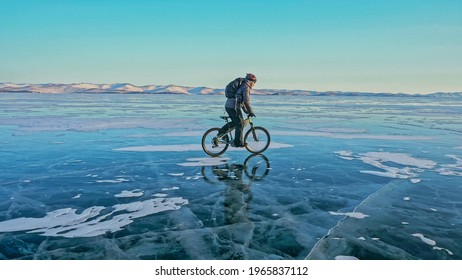 Man is riding bicycle on the ice. Ice of the frozen Lake Baikal. Rider is dressed in black down jacket, cycling backpack, helmet. Tires on covered with special spikes. Traveler boy is ride cycle. - Powered by Shutterstock