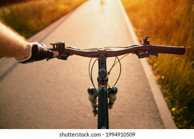 A man riding a bike. Holding bike handlebar with one hand in a sports glove with sunlight at the top. Concept of summertime outdoor leisure sport activity. First-person view bicycle riding.