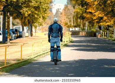 Man riding an electric unicycle in city park on bright autumn day, wearing protective gear for safety riding, eco-friendly transportation, leisure in the outdoors. EUC rider wearing protective armor - Powered by Shutterstock